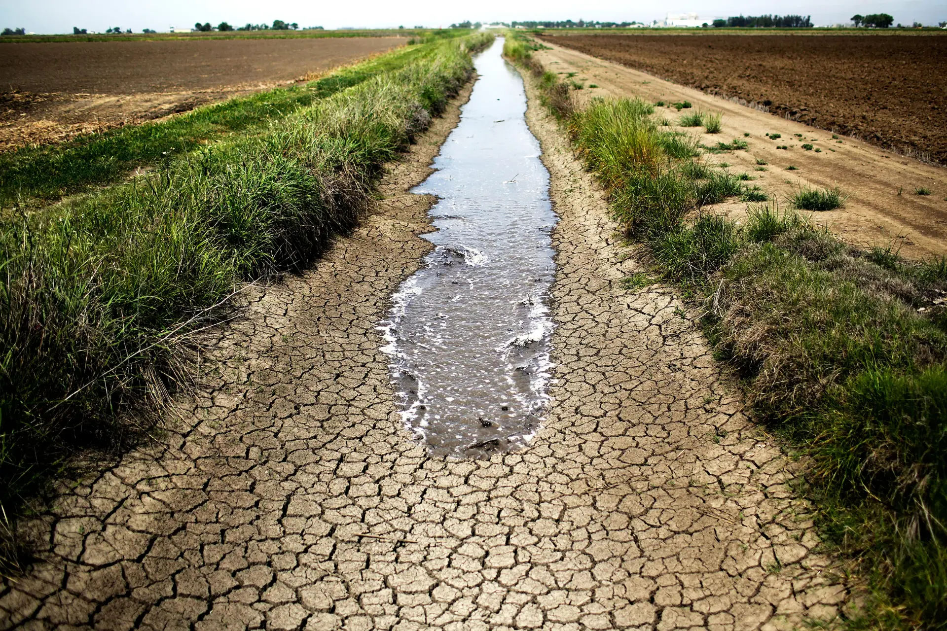 Cracked irrigation canal running through arid farmland